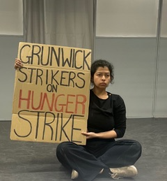 A woman holds a placard that says "Grunwick Workers on Hunger Strike"